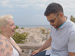 A busty blonde in a summer dress walks along the road, looking for a ride.